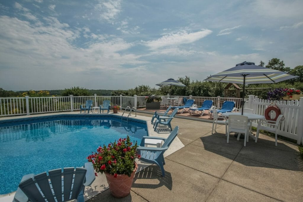 Outdoor Pool in Camden at Glen Cove Inn - pool chairs with an umbrella and planters with a blue sky